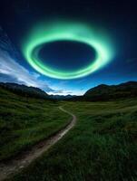 A trail leads through a green valley under a ring of aurora lights photo