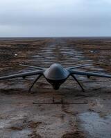 A stealth drone sits on a runway in a desolate landscape photo