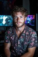 Man with curly hair wearing a floral shirt in front of computer monitors photo