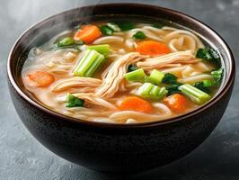 A steaming bowl of chicken noodle soup with vegetables photo