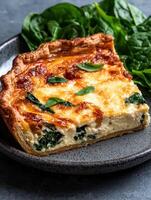 A slice of spinach and cheese quiche with a flaky crust, served with fresh spinach photo
