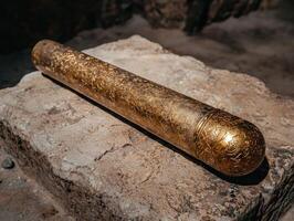 A golden cylinder with intricate carvings rests on a stone surface photo