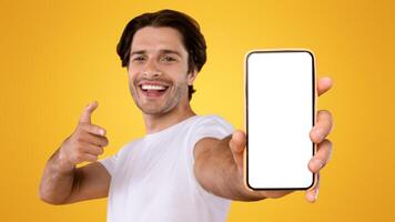 Check This Website. Portrait of smiling male holding smart phone with white blank screen in hand, showing device close up to camera and pointing finger at gadget with empty free space for mock up photo