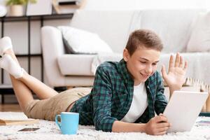 Schooler having videochat with friends on digital tablet from home, communication during isolation, free space photo