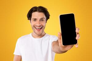 Mobile Application Ad. Portrait Of Excited Man Showing Smart Phone Black Empty Screen Recommending App Standing Over Yellow Orange Studio Background. Cellphone Display Mock Up, Check This Website photo