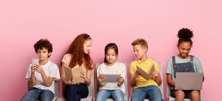 Elearning concept. Diverse schoolchildren using tablet, laptop, smartphone and books to study online on chairs over pink background photo
