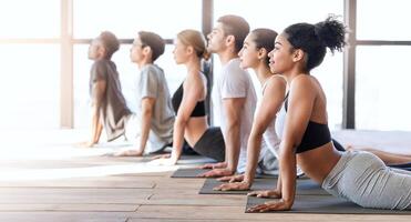 Yoga group members doing cobra pose while excercising in modern loft studio, lying on mats in a row, side view with free space photo