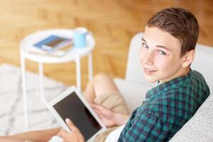 Teen guy using digital tablet with empty screen, home interior, top view, copy space photo