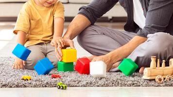 Family leisure. Cute little boy playing colorful blocks with happy daddy, spending weekend together, sitting on floor at home interior photo