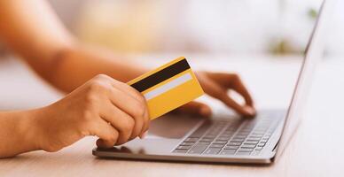 Ecommerce Concept. Side view of unrecognizable african american woman holding credit card in hand and using laptop, typing security information on keyboard, blurred background, selective focus photo