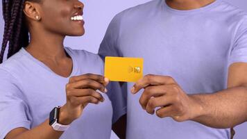 Easy Digital Payment. Happy Black Couple Hugging, Holding And Showing Golden Credit Card Close Up To Camera, Looking At Each Other, Recommending Banking Service Over Purple Violet Studio Background photo