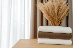 Stack of folded towels on a wooden table with wheat and curtains in the background photo