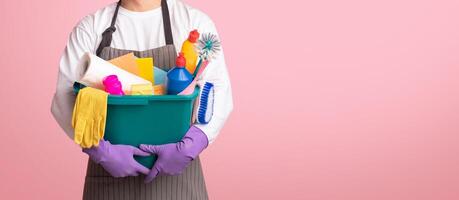 Bucket with cleaning supplies and tools in hands of unrecognizable man in apron standing on pink background, cropped image, panorana with free space photo