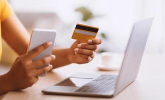 Making Financial Transaction. Closeup of unrecognizable black lady holding credit card and smartphone, sitting at desk with laptop computer, blurred background. Online Shopping And Payment Concept photo