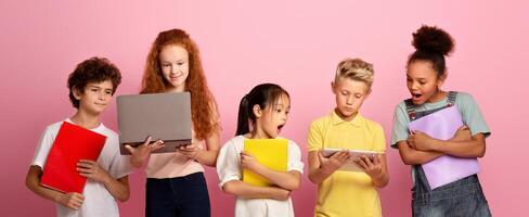 Portrait of multiethnic schoolchildren with notebooks using tablet and laptop to study over pink background photo
