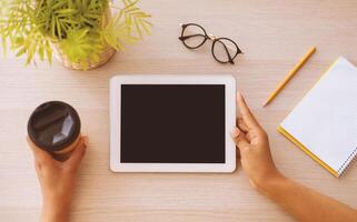 Modern Technology Concept. Top above high angle view of african american woman using digital tablet with empty black blank screen for template mock up, sitting at desk, drinking coffee, copy space photo