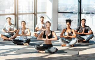 Yoga Session. Young people doing group meditation in modern studio, sitting in lotus position with eyes closed, copy space photo