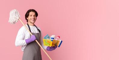 Spring-Clean Service Worker. Portrait Of Happy Man Holding Mop And Bucket With Cleaning Tools, Standing Over Pink Studio Background, Free Space photo