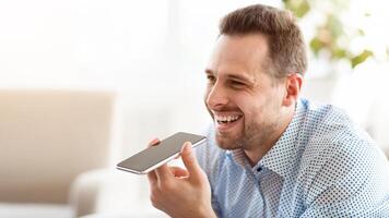 Voice Search. Smiling guy using smart phone voice recognition to send message, holding gadget near mouth photo