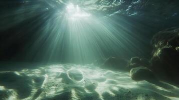 Underwater sunlight creating light rays through turquoise water onto sandy seabed photo