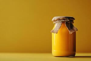 Glass jar with honey and rustic fabric cover on yellow background photo