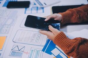 A person is using a smartphone on a table with blueprints photo