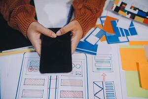 A person using a smartphone on a desk with a lot of paper and other materials photo