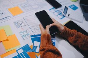 A person is using a smartphone on a table with a lot of paper and other items photo