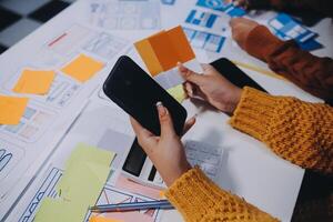 A person is using a cell phone while sitting at a table with paper and sticky notes photo