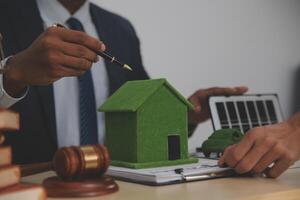 A man in a suit and tie is signing a contract with a green house model photo