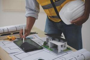 A man in a hard hat and safety vest is working on a blueprint photo