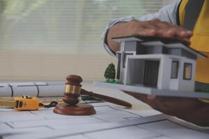 A man holding a model of a house and a gavel on a table photo