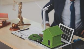 A man in a suit sits at a desk with a laptop and a green house on it photo