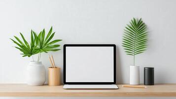 A laptop sits on a wooden desk with a vase of green leaves photo