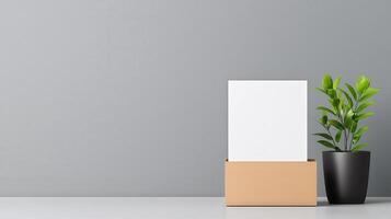 A white box with a plant in a black pot sits on a grey table photo