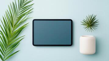 A tablet is on a table next to a plant and a white vase photo