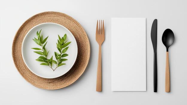 A white plate with a leaf on it sits on a table with a fork, knife, and spoon photo