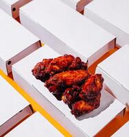 Juicy chicken wings in white boxes on an orange background photo