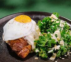 Delicious breakfast croissant topped with egg and side salad photo
