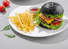 Black burger with golden fries and fresh tomatoes on a plate photo