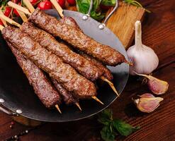 Grilled skewers of tender meat on a wooden table with vegetables photo