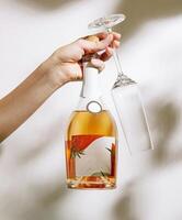 Hand holding a bottle of wine and a glass in a bright setting photo