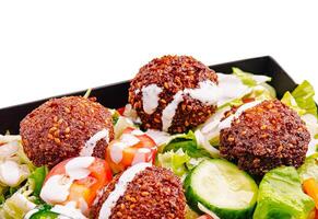 Fresh salad with crispy falafel and drizzled sauce served on plate photo