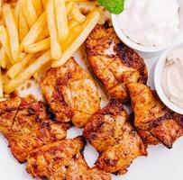Grilled chicken with fries and dipping sauces on a plate photo