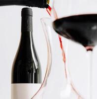 Pouring red wine into a glass near a bottle on a table photo