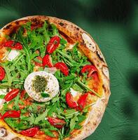 Fresh pizza topped with arugula and cherry tomatoes on a green table photo