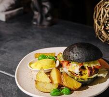 Gourmet black bun burger with seasoned potato wedges and sauce photo