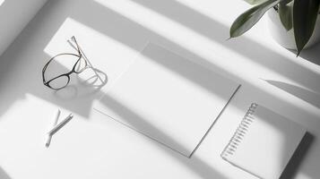 An overhead view of a white desk with a notebook, pen, and glasses photo