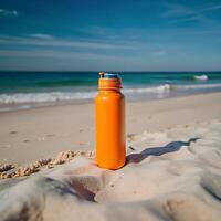 Orange Water Bottle on Sunny Beach Sand Next to Ocean Waves on a Beautiful Day photo