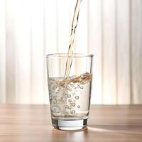 Liquid being poured into a clear glass on a wooden table with a blurred background photo